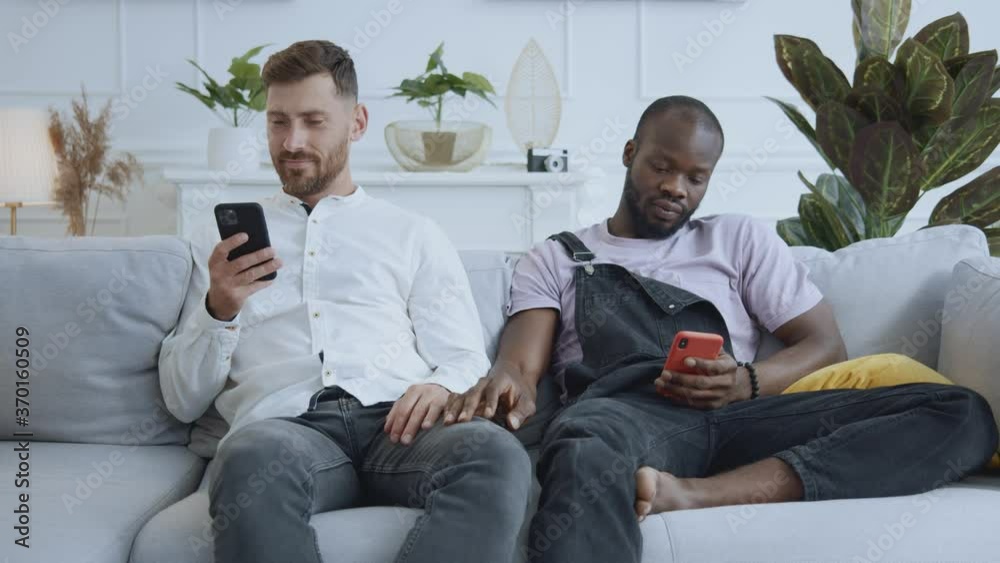 African american man flirting with his busy boyfriend using cellphones together. Offended caucasian man boyfriend turning him back. Relationships problems. African american man flirting with his busy boyfriend using cellphones together. Offended caucasian man boyfriend turning him back. Relationships problems.