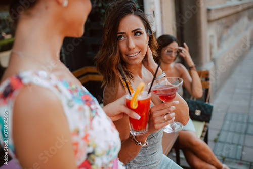 Three beautiful young caucasian women in short summer dresses are sitting and drinking cocktails in the cafe garden. Girls at parties