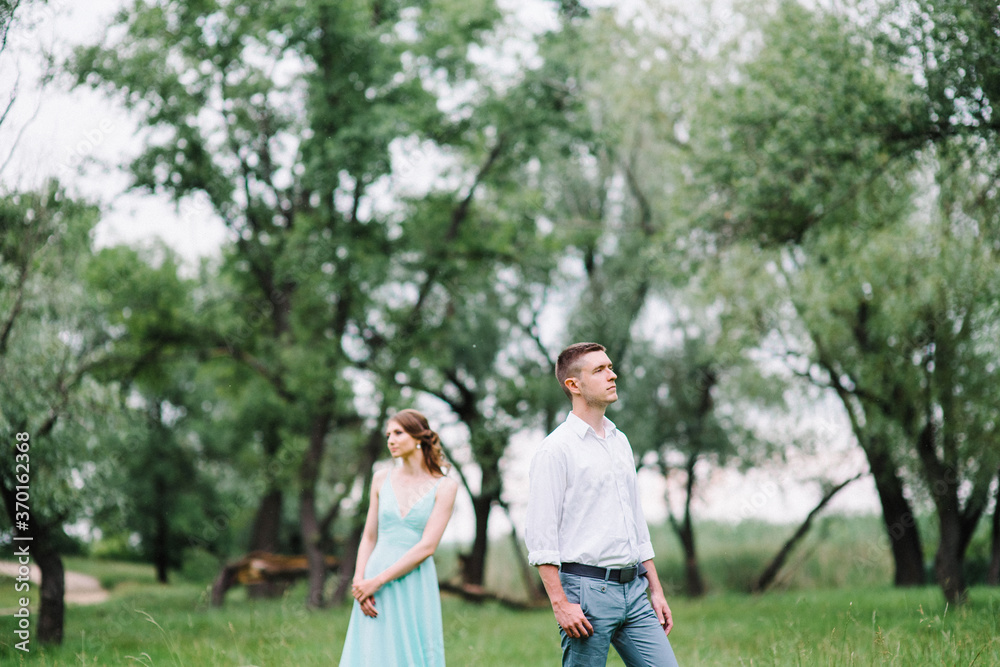 happy guy in a white shirt and a girl in a turquoise dress are walking in the forest park