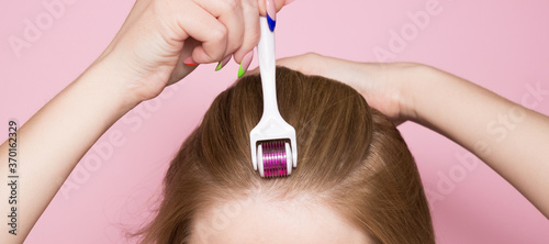 Mesotherapy for hair using a mesoroller. Care for the scalp, hair growth, against hair loss. A woman with a mesoroller on her hair on a pink background.