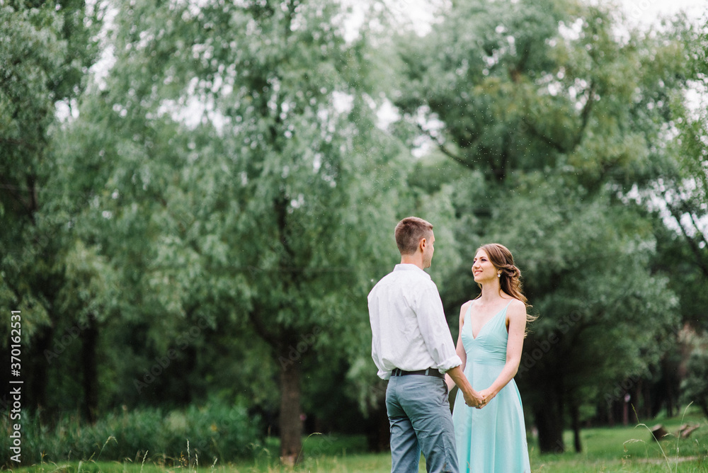 happy guy in a white shirt and a girl in a turquoise dress are walking in the forest park happy guy in a white shirt and a girl in a turquoise dress are walking in the forest park