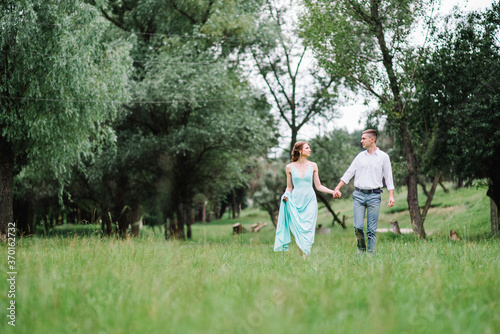 happy guy in a white shirt and a girl in a turquoise dress are walking in the forest park