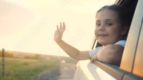 happy girl kid child smile leaned out of a car window waving hand. happy family travel journey concept. daughter sister looks out of a car window. little happiness girl drive road to lifestyle