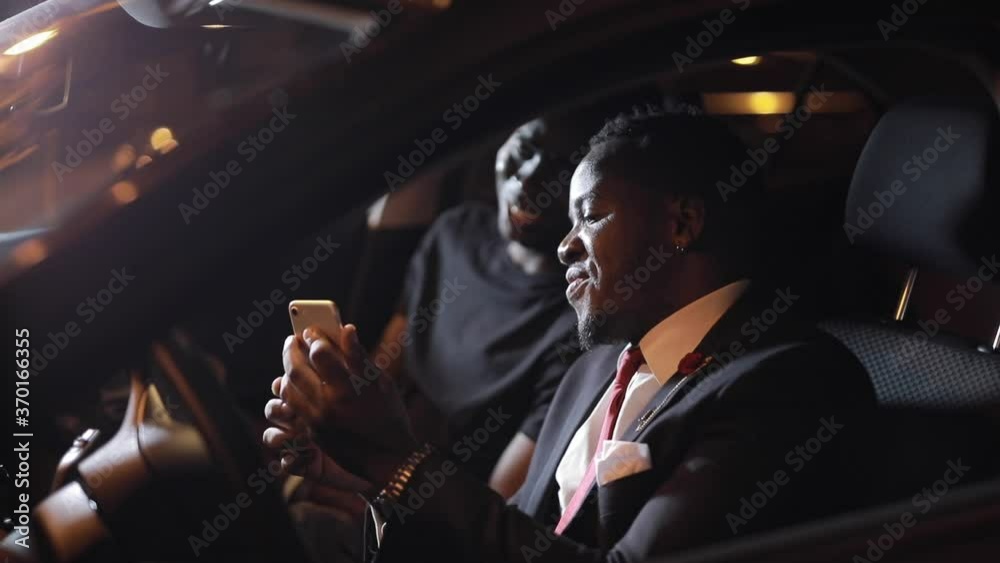 African men friends looks into smartphone in the car at night African men friends looks into smartphone in the car at night