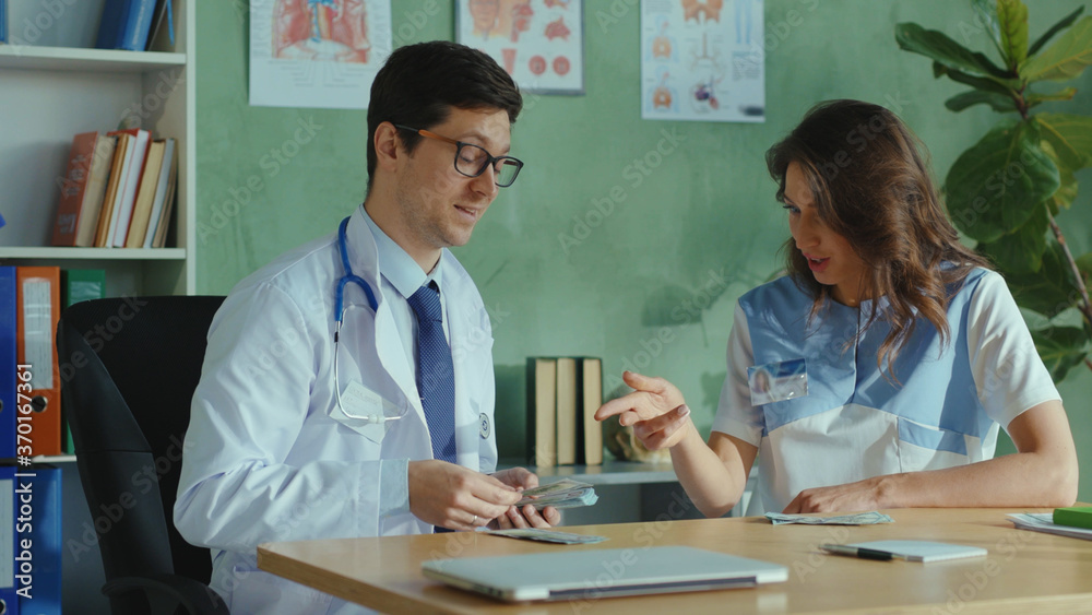 Cunning excited caucasian doctor and nurse assistant counting and sharing money earnings after workshift. High paid job. Corruption in medicine. Cunning excited caucasian doctor and nurse assistant counting and sharing money earnings after workshift. High paid job. Corruption in medicine.