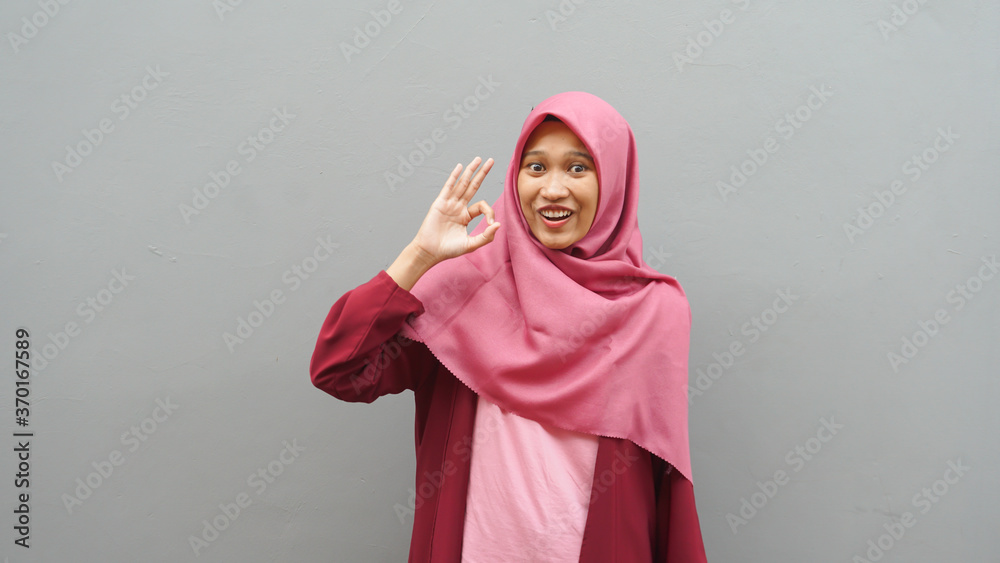 Portrait of young Asian muslim lady wearing hijab shows thumbs up gesture, smiling happy face, approved OK sign