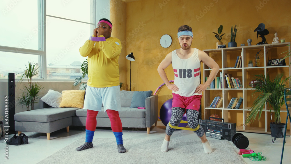 Sports parody. Comical funny unfit retro looking young men training with resistance  bands doing wrong exercises having fun home workout. Stock Photo | Adobe  Stock