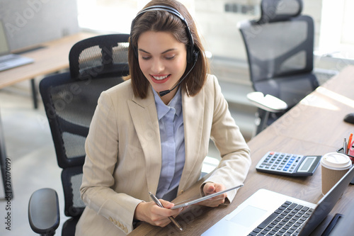 Cheerful female manager sitting at office desk and performing corporate tasks using wireless connection on digital gadgets. © ty