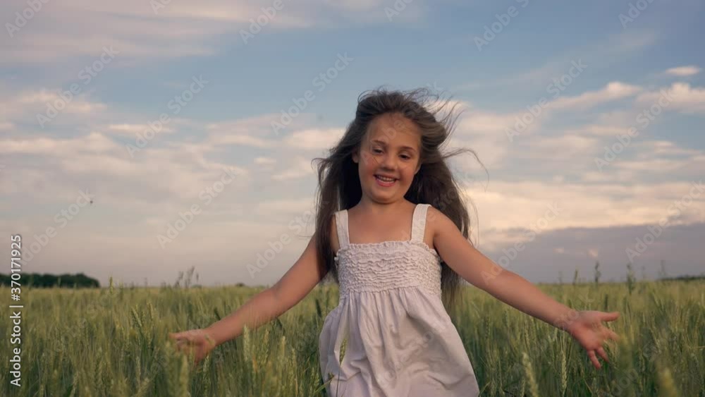 A happy little girl runs through a wheat field with her arms outstretched. A child enjoys the fresh air in the countryside. Happy child in the Park. Childhood dream