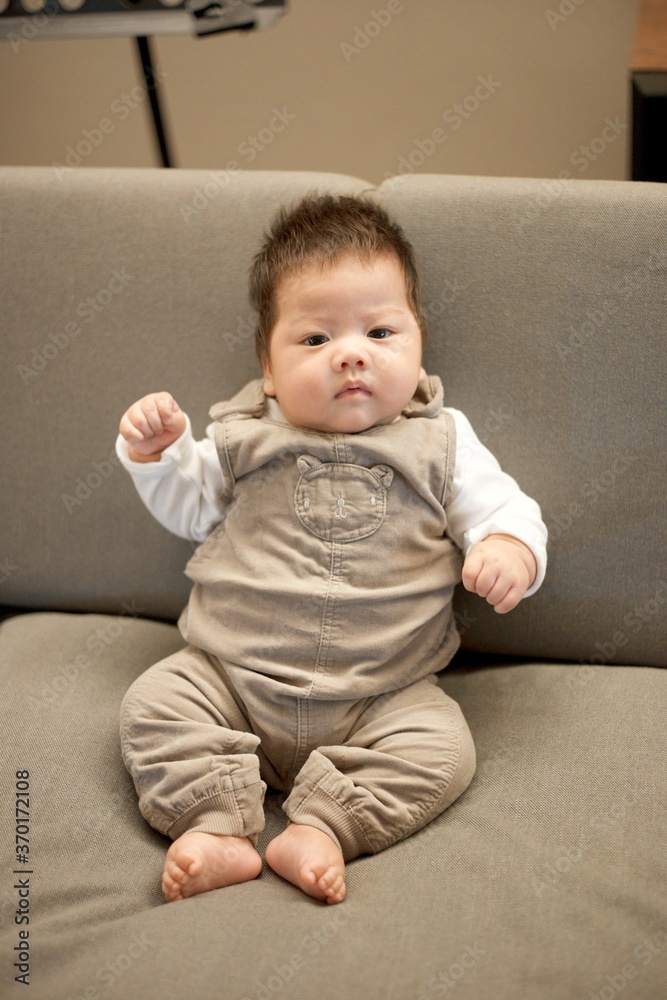Cute baby boy in brown overall outfit sitting on sofa. Cute baby boy in brown overall outfit sitting on sofa.