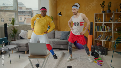 Joyful and funny retro style unfit sportsmen doing fun sports routine dancing with exercises into music during home training. Multi-ethnic fitness team. photo