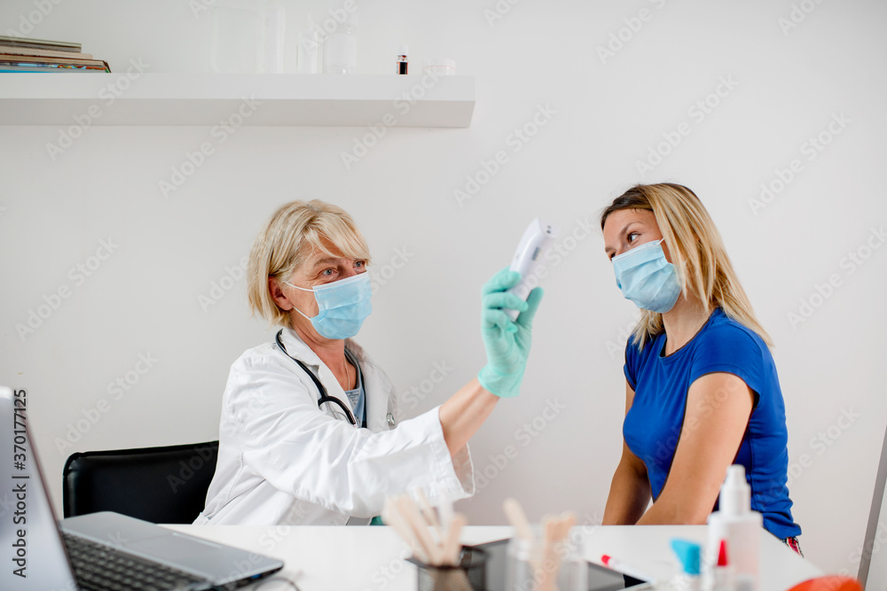 Obraz premium Female doctor doing medical exam to a young woman. They are wearing a protective face mask.