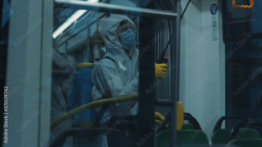 Public transport decontamination. Janitor in protective chemical suit cleaning the tram disinfecting walls for virus prevention. Outbreak of coronavirus. Sanitary.