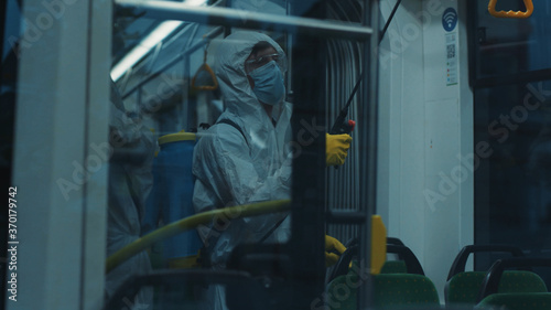 Public transport decontamination. Janitor in protective chemical suit cleaning the tram disinfecting walls for virus prevention. Outbreak of coronavirus. Sanitary.