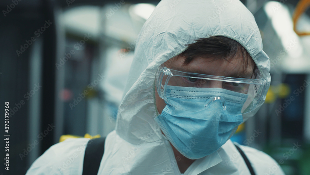 Sanitation worker in chemical protection suit standing in empty tram. Portrait young professional cleaner look at camera while disinfecting public transport. Sanitation worker in chemical protection suit standing in empty tram. Portrait young professional cleaner look at camera while disinfecting public transport.