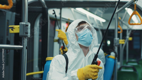 Professional virologist in white suit disinfecting walls of public transport tram with cleaning chemicals for virus prevention. Coronavirus. Pandemic. Decontamination.