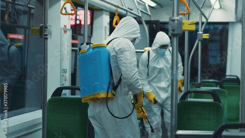 Couple of professional cleaners disinfecting empty tram, spraying chemicals on walls and floor, cleaning public transport for sanitary measures. Pandemic.