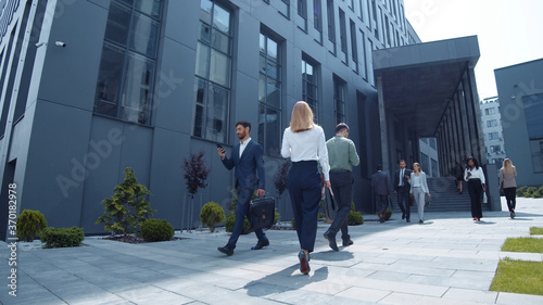 Multi-ethnic young business persons corporate workers walking outside company in modern district downtown. Office people diversity. Urban lifestyle.