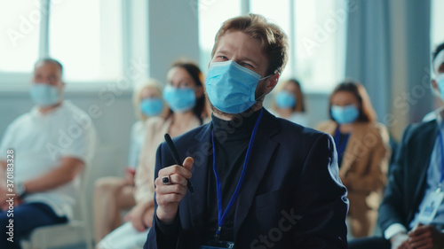 Corporate staff workers with masks participate in professional business seminar. Attentive young entrepreneur making notes listening to speaker. Pandemic. Business people.