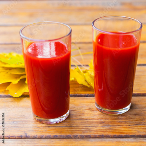 Tomato juice in a glass cup and yellow autumn leaves on a wooden table. Selective focus.