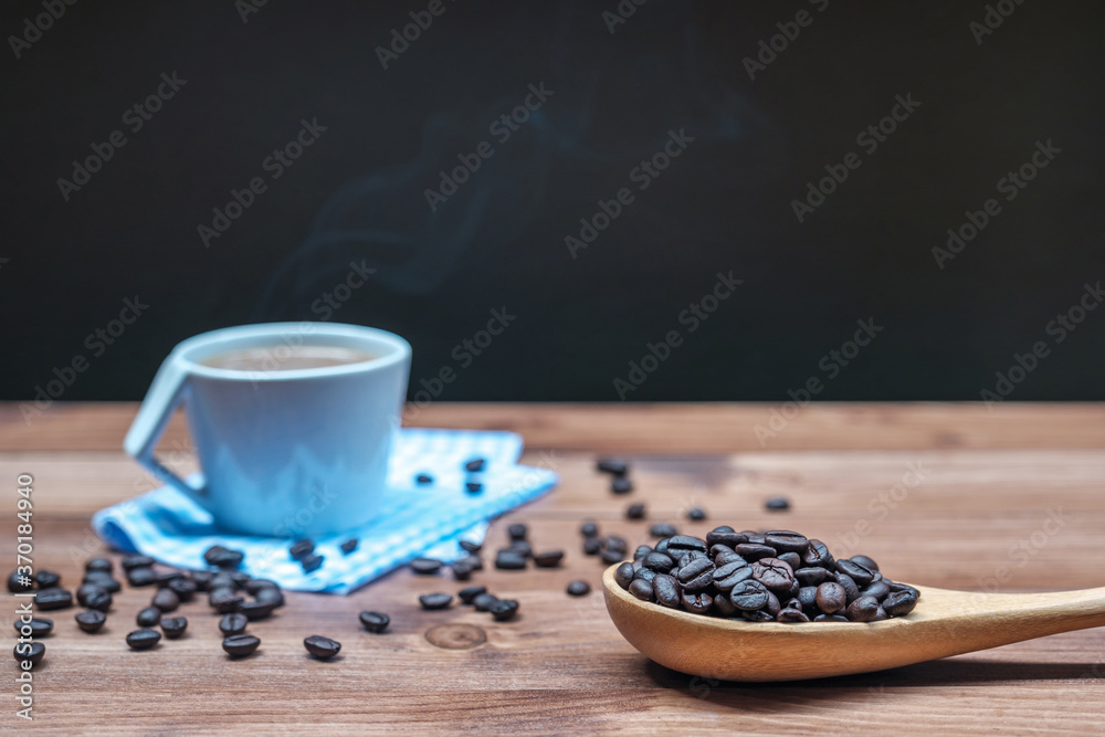 Roasted coffee beans on wood spoon and hot coffee in cup with smoke on the wood floor.