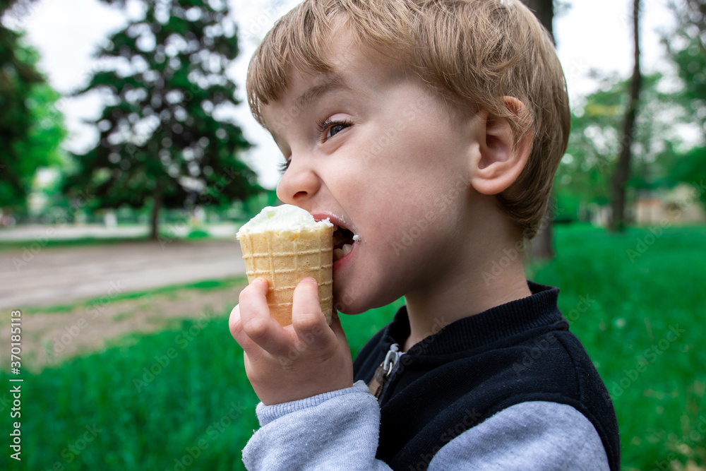 three year old child eating ice cream in summer park. green grass and trees on the background of the child. walks with parents. favorite desserts concept three year old child eating ice cream in summer park. green grass and trees on the background of the child. walks with parents. favorite desserts concept