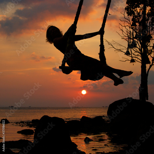 A girl's silhouette on a swing against the sea during sunset in Thailand
