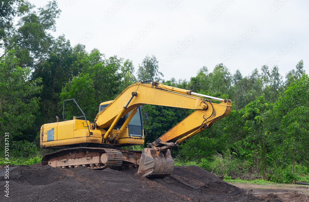 Yellow excavator parked on a pile of crushed stone on natural forest background.