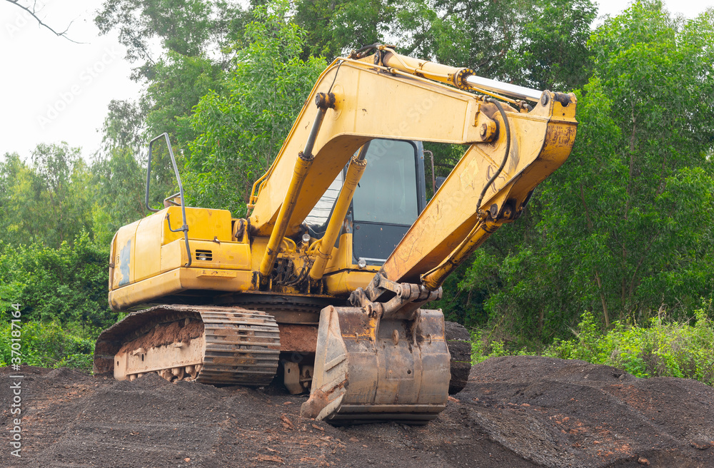 Yellow excavator parked on a pile of crushed stone on natural forest background. Yellow excavator parked on a pile of crushed stone on natural forest background.