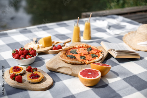 Delicious summer picnic in nature near the lake. Picnic with pizza  sweets  berries and reading books. Outdoor picnic. Focus on food