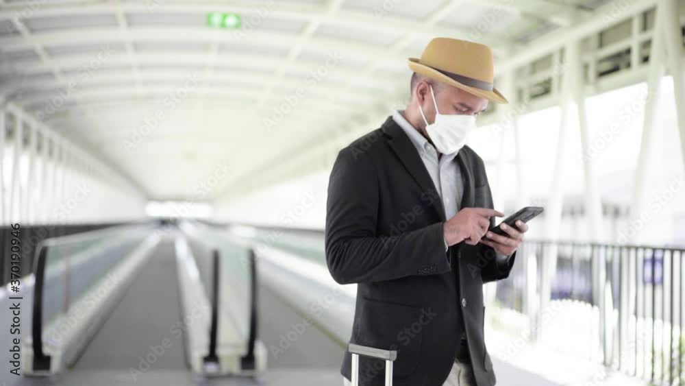 Young asian business tourist live in airport, He wearing face mask for protect virus air pollution on safety travel and use mobile phone while standing with his bag. Slow Motion Shot. Young asian business tourist live in airport, He wearing face mask for protect virus air pollution on safety travel and use mobile phone while standing with his bag. Slow Motion Shot.