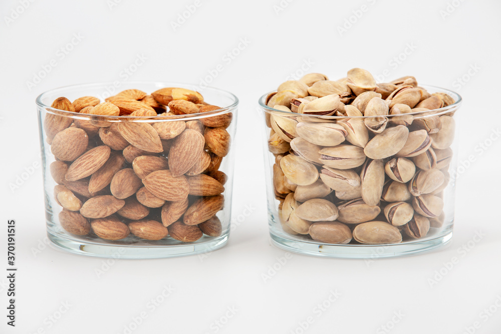 Pile of salted pistachios and almonds in glass bowl on white background.