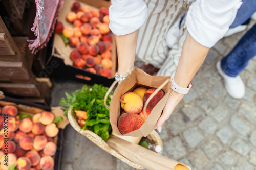 Unrecognizable woman hands holding paper bag with organic peaches outdoors at farmers market.