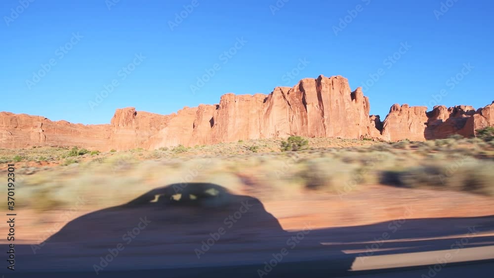 Pov point of view panning driving vehicle side view shot on arches scenic drive at Arches National Park in Moab, Utah at sunrise with canyons rock formations and car shadow on road trip