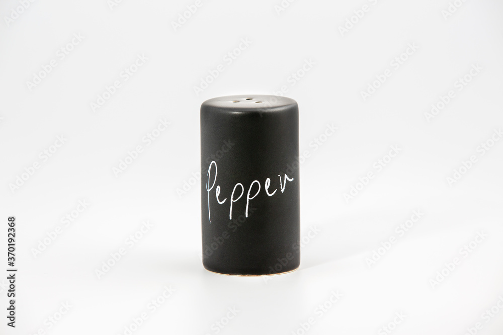Black porcelain pepper shakers on the white background with some salt and copy space. Simple and elegant, minimalist design. Black porcelain pepper shakers on the white background with some salt and copy space. Simple and elegant, minimalist design.