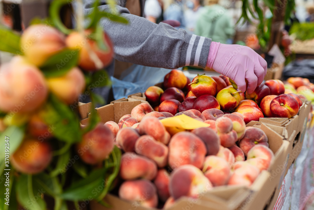 Close up of seller's hads in protective gloves putting organic peach in mesh bag. Buyer chooses peaches. New social rules after pandemic. Close up of seller's hads in protective gloves putting organic peach in mesh bag. Buyer chooses peaches. New social rules after pandemic.