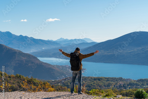 A traveler with a backpack stands on the top of the mountain and holds his hands to the sides