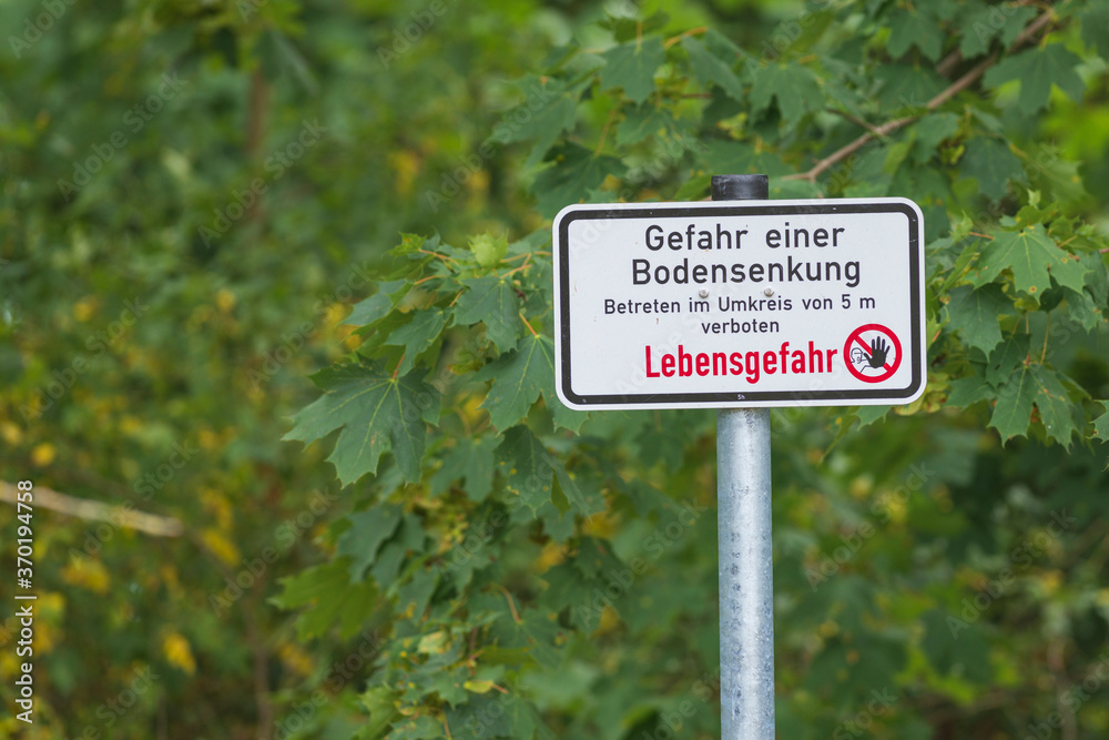 Ein Warnschild in einer Tagebaufolgelandschaft mit der Aufschrift Gefahr einer Bodensenkung  , Betreten im Umkreis Umkreis von 5 m , Lebensgefahr
