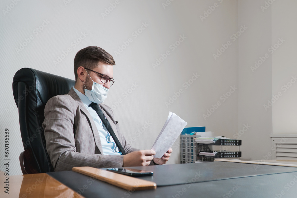 Young businessman in glasses and face mask working in his personal office. Business during quarantine. Young businessman in glasses and face mask working in his personal office. Business during quarantine.
