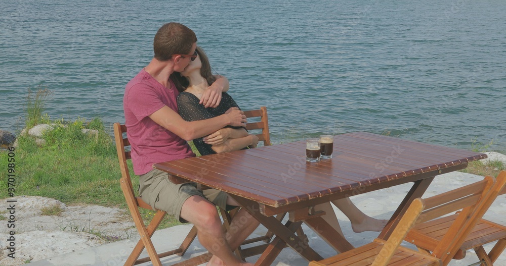 Couple in love sitting by the marina near the sea. Admire the scenery, hug, kiss, talk to each other and have fun