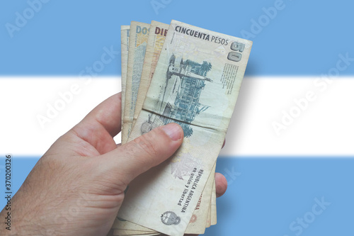 Man's hand holding Argentine money. Banknote Argentine money. Isolated on background with blurred Argentine flag. Finance concept.