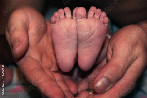 Men's hands hug the heels of a newborn baby