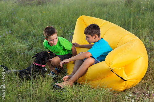 two boys outdoors sitting on yellow air couch playing with dog, summer concept photo