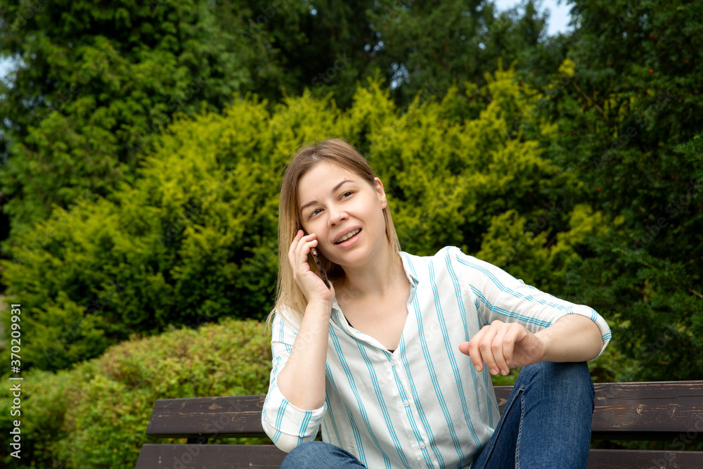 girl with blond hair talking on the phone sitting on a bench in the park. girl with blond hair talking on the phone sitting on a bench in the park.