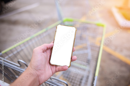 Holding a smartphone white screen with blurred shopping cart background.