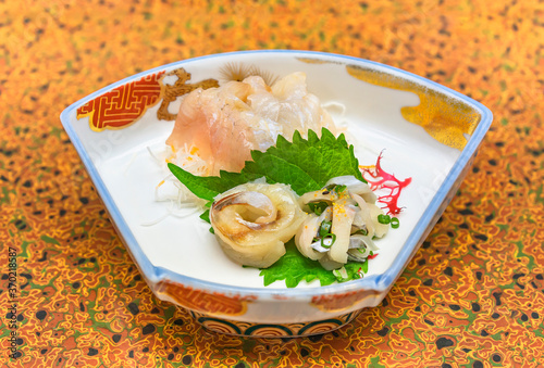 Raw sashimi high-class japanese cuisine of fresh Sayori needlefish, Madai seabream and Hirame halibut in a trapezoid dish plate with Gracilaria red algae, shiso leaves and julienne of daikon radish. photo