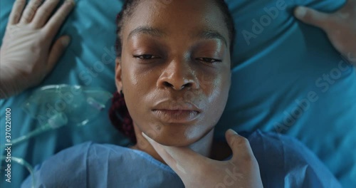 Top view of afro american girl heart beat stopped while she lying on medical stretcher. Close up of ill woman dying while riding in ambulance to hospital. Concept of illness