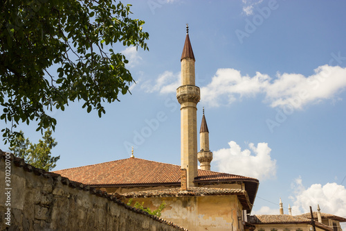 Summer sunny day. The roof of the mosque with high minarets. Bright green foliage