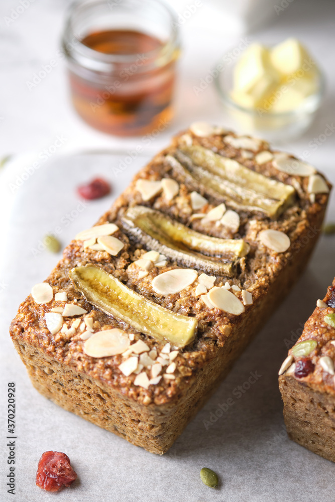 Loaf of Vegan Oatmeal Banana Bread topped with nut, seed, almond slide and banana set on cafe table.
