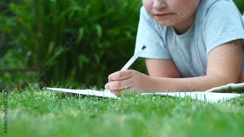 close up child hands writing thoughts and dreams in a diary book laying on grass at nature. dreamy child dreaming outdoors. Thoughtful schoolboy making notes in a notebook
